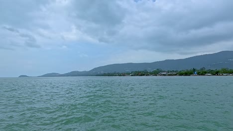 Calm ocean waves under a cloudy sky with distant hills in Koh Samui, Thailand. Gentle camera movement captures tranquil seascape