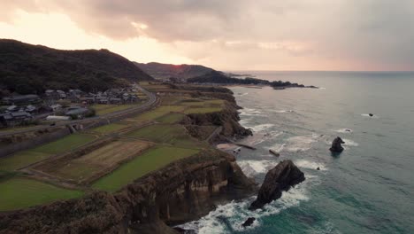 Acantilado-Aéreo-Japonés-En-La-Playa-De-Kyotango,-Kansai,-Japón,-Campos-Con-Mar-Y-Puesta-De-Sol,-Espectacular-Cielo-Degradado,-Paisaje-De-Hora-Dorada