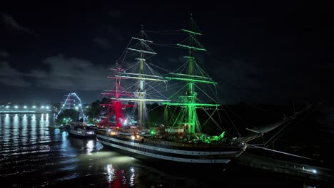 drone shot showing amerigo vespucci navy ship lighting in red white green colors at night - docking at harbor of dominican republic