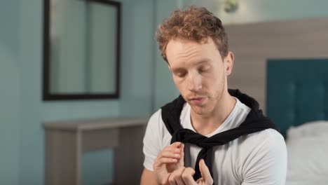 Young-handsome-man-takes-care-of-his-nails-while-sitting-in-the-bedroom