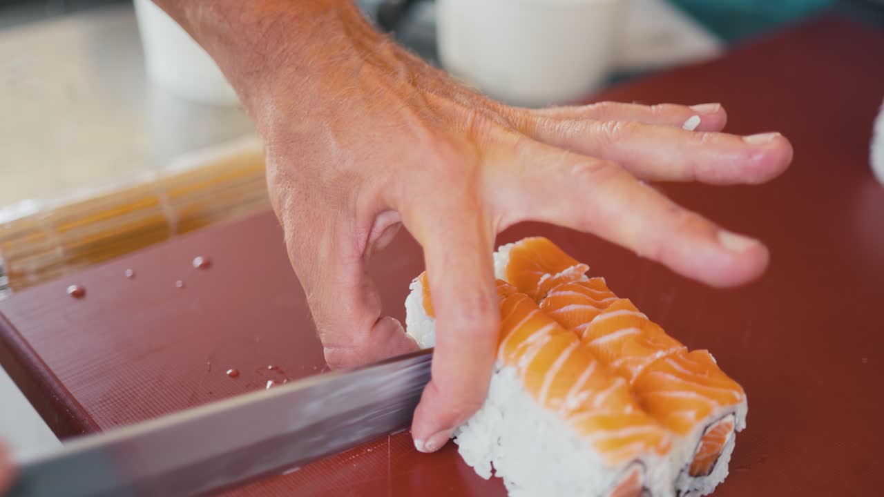 un chef profesional corta un rollo de sushi con salmón en trozos, haciendo rollos de uramaki, cocina tradicional japonesa