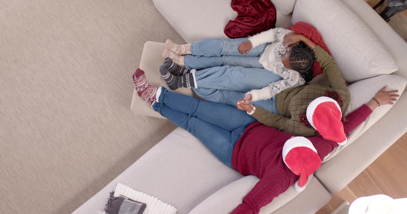 Famiglia afroamericana sdraiata su un divano chiaro, un adulto alza il braccio guidando un giovane che si appoggia per Natale.