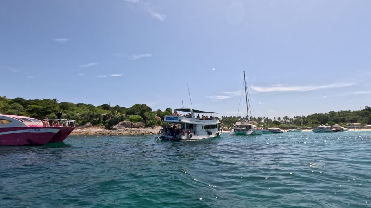 Tour boats glide on clear blue water near lush Phuket coast, captured with smooth panning