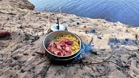 Cooking pasta with tin meat on a campfire outdoor, survival cook on fire