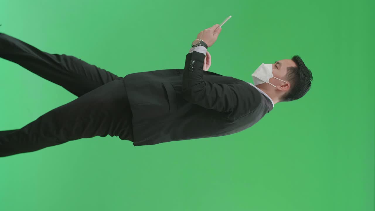 Side View Of Asian Business Man Use Tablet While Walking On Green Screen Chroma Key, Wear Medical Mask