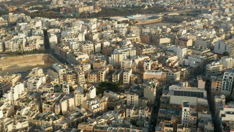 Beige-Brown-Apartment-Blocks-in-Hot-Area-in-Sunlight-on-Malta-Mediterranean-Island,-Aerial-Wide-View-Drone-slide-left-Perspective