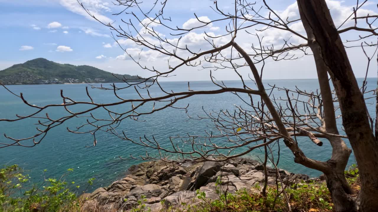A serene view of the ocean from a rocky cliff in Phuket, Thailand, with lush greenery and clear blue skies