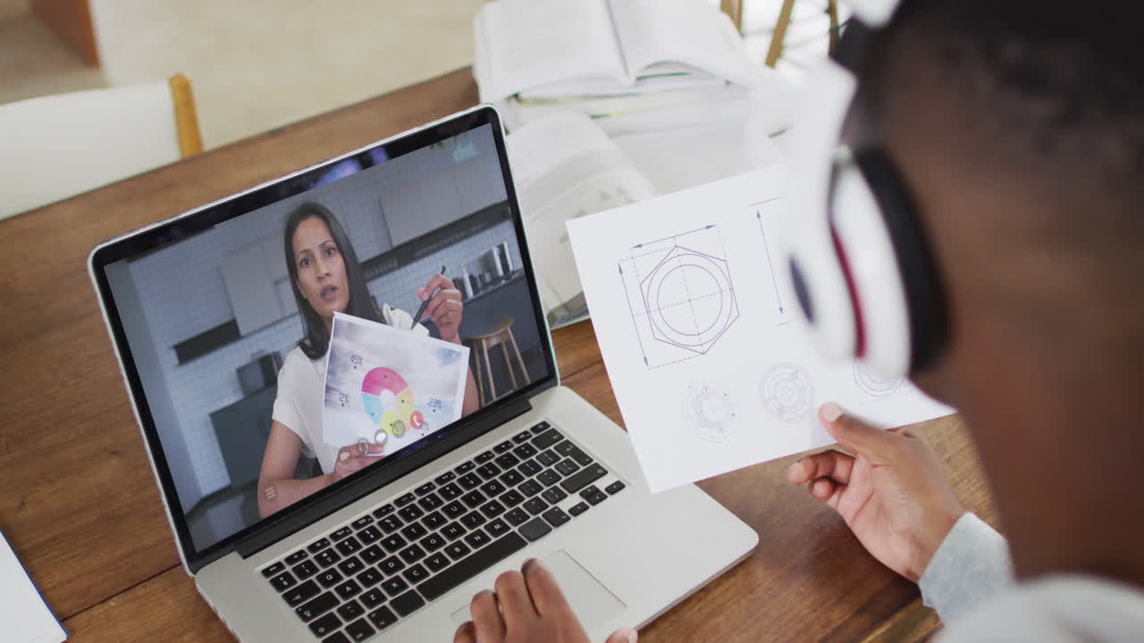 estudiante universitario afroamericano que sostiene notas mientras hace una videollamada en una computadora portátil en casa