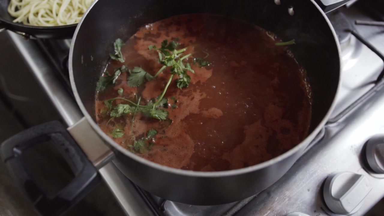 Primo piano di salsa di pomodoro che sobbolle in una pentola con erbe fresche sul fornello della cucina mentre si prepara un pasto fatto in casa durante la cottura in una cucina domestica.