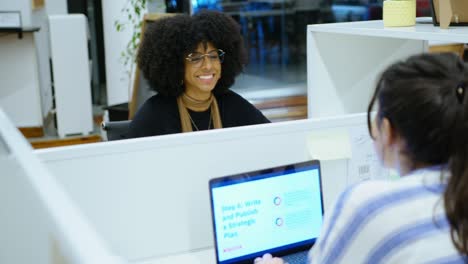 female colleagues sitting at office cubicles and chatting during workday