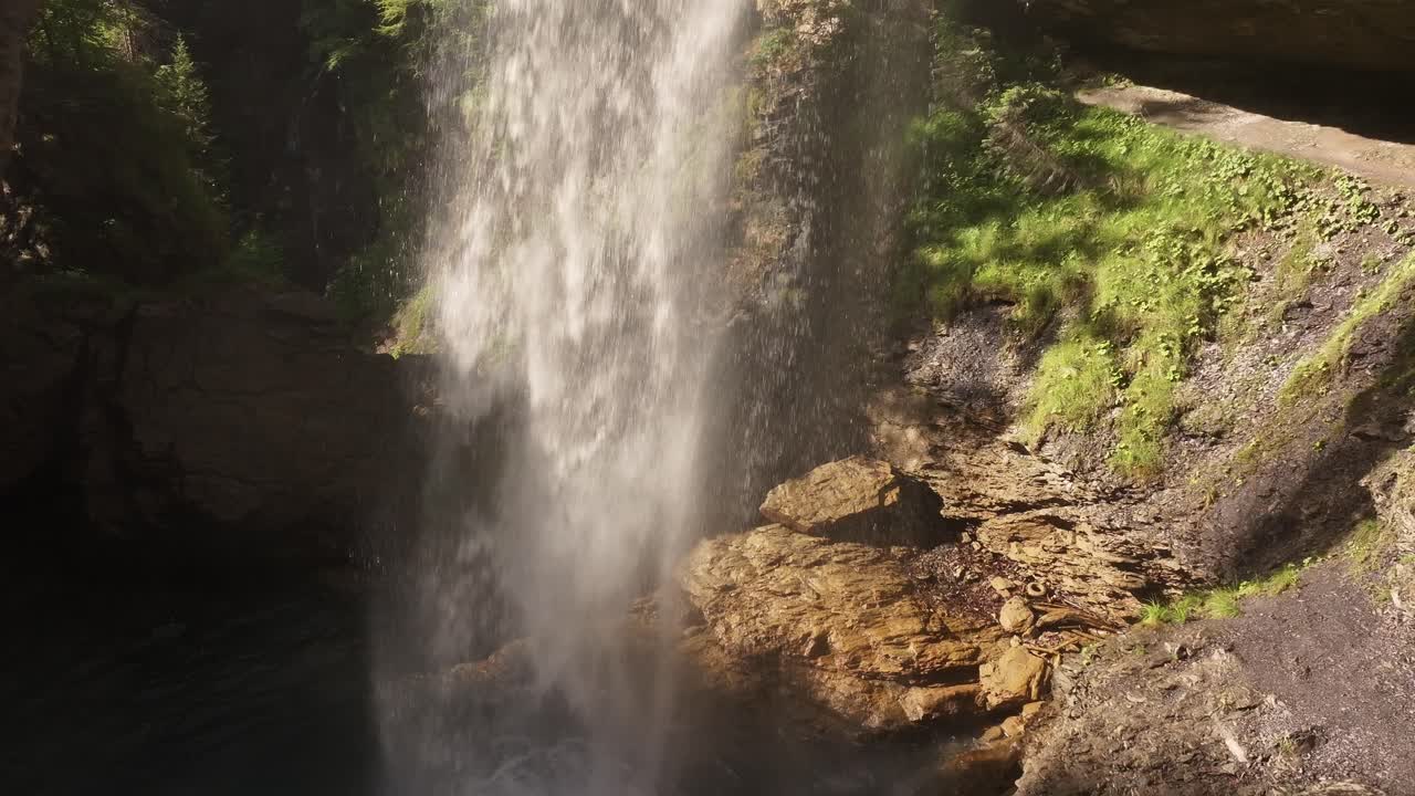 A powerful stream of water creates the Bergli Stüber Waterfall, plunging from a large grotto carved into the rocky cliffs of Fätschbach in Glarus Süd, Switzerland