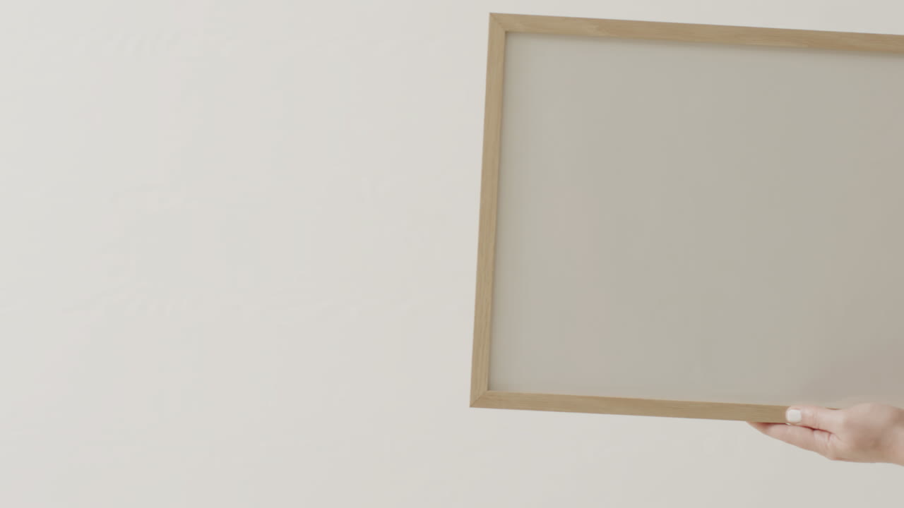 mano de mujer caucásica sosteniendo el marco con espacio de copia en fondo blanco contra la pared blanca