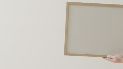mano de mujer caucásica sosteniendo el marco con espacio de copia en fondo blanco contra la pared blanca