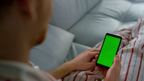 app user holding chroma key smartphone closeup. unknown man lying scroll feed.