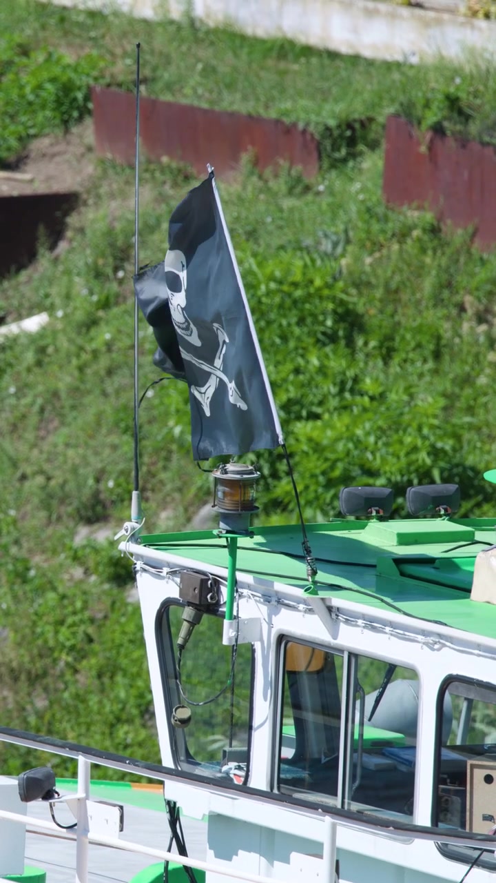 Bandiera pirata nera sventola sulla cima di una barca dal tetto verde ormeggiata lungo il fiume in pieno giorno, Praga, Repubblica Ceca