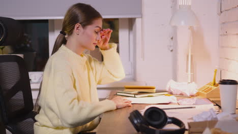 sleepy young woman turning on the tablet and writing something on paper while sitting at desk in the office