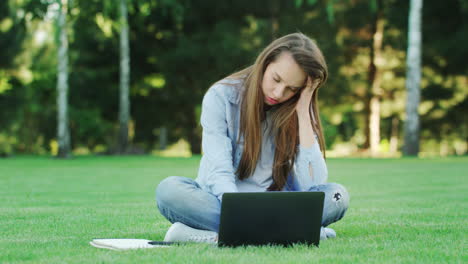 Mujer-Enfocada-Usando-Un-Cuaderno-Para-Trabajar-En-Línea-Sobre-Hierba-Verde-En-El-Parque-De-Verano