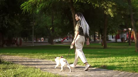 Purebred-pug-running-in-the-park-with-dreadlocks-female-owner-leading-the-leash-in-summer