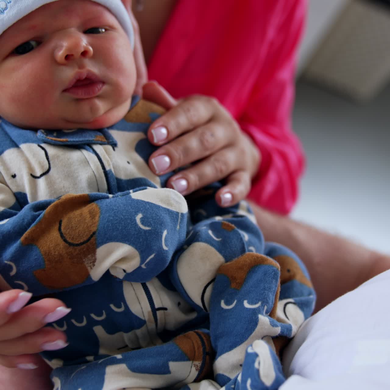 Tiny newborn wearing blue romper and white cap. Loving mom holding her son and kissing him on the head. Close up