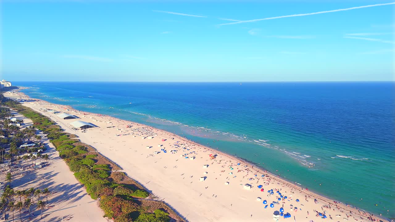 Drone hovers over the sand, rotating 360° to reveal South Beach in every direction—ocean waves, golden shoreline, Miami skyline, and the endless coastal view stretching north and south.