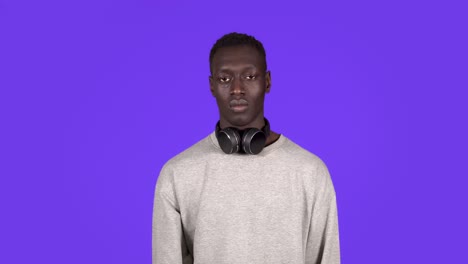 Porträt-Eines-Jungen-Afroamerikanischen-Mannes-In-Weißem-Hemd,-Der-Isoliert-Auf-Blauem-Hintergrund-Im-Studio-Posiert.-Menschen-Emotionen-Lifestyle-Konzept.-Zeigt-Stopp-Geste-Mit-Der-Hand,-Kopfhörer-Am-Hals