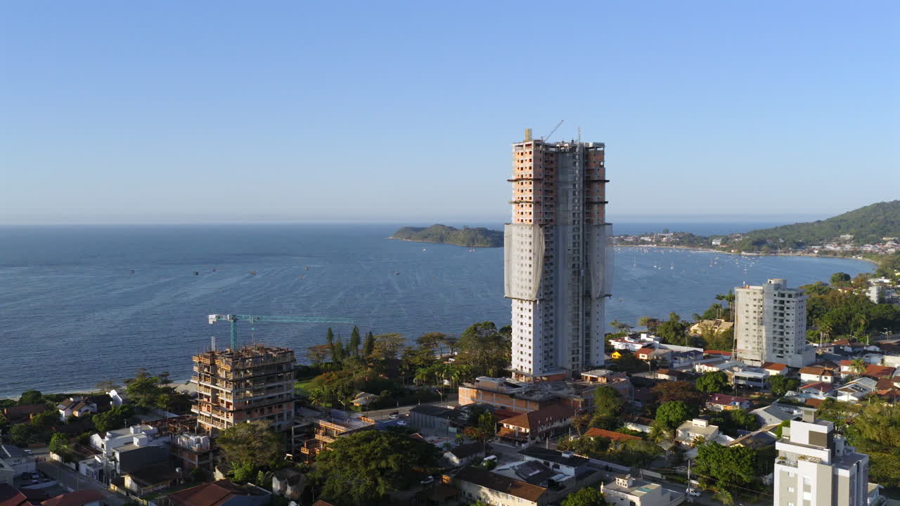 Drone glide beside oceanfront construction in Penha, with boats harbor nearby during afternoon. General view with distant horizon