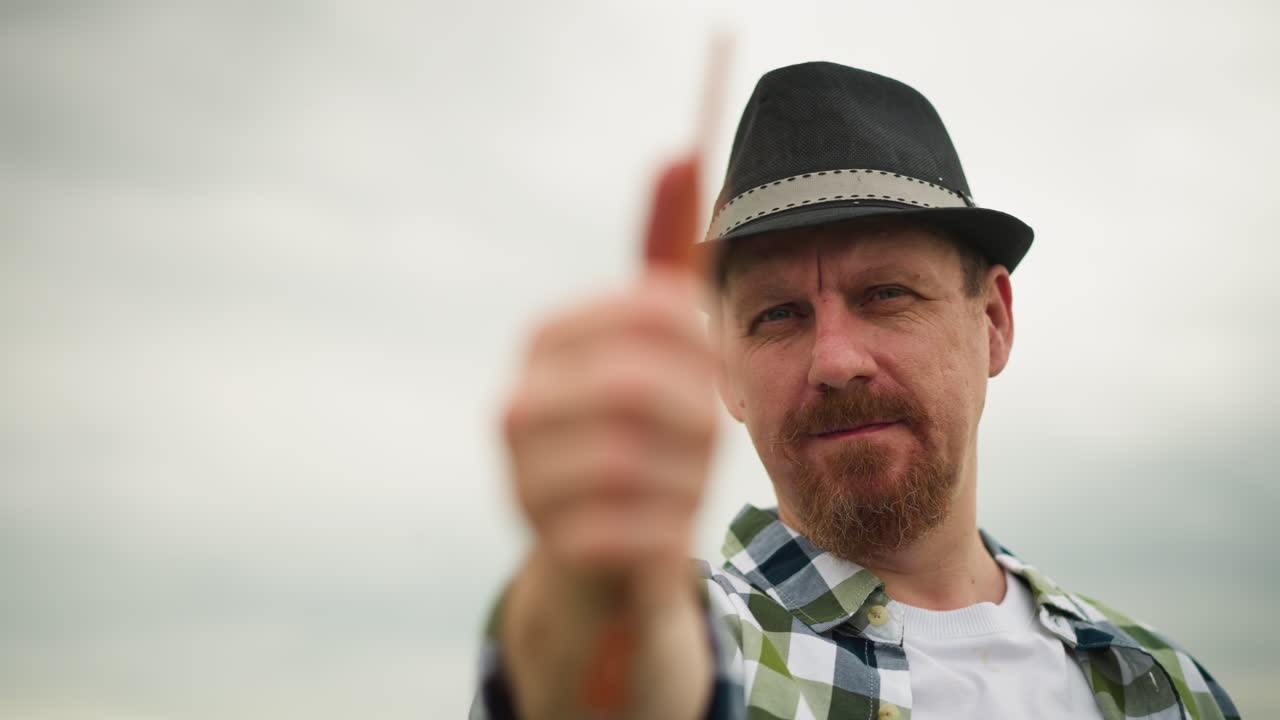 Close-up of a sculptor in a checked shirt and hat, holding a brush with intense focus, against a blurred background