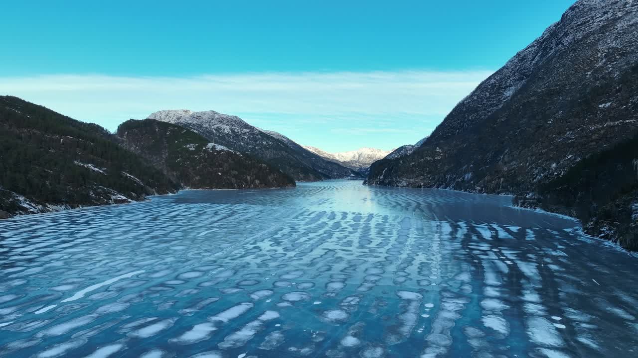 Luftaufnahme, die sich von der Eisfläche erhebt und den gefrorenen Eidsfjord enthüllt, der sich unter klarem Winterhimmel in Norwegen in Richtung der Berge erstreckt.