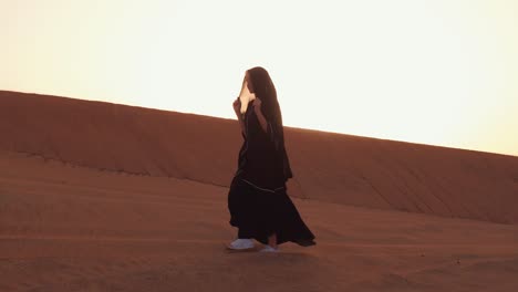 mujer musulmana de pie cerca de la mezquita en el desierto. viento fuerte oriente medio paz sin guerra