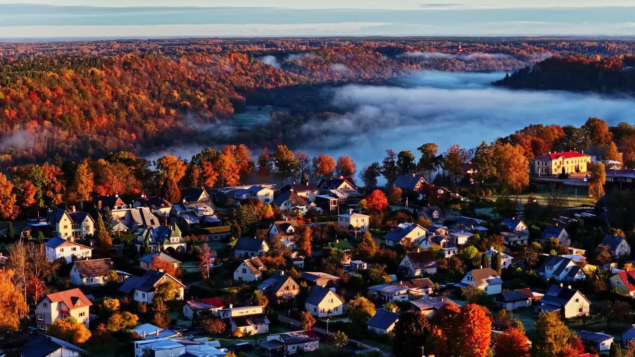 Aerial sunrise over Sigulda, Latvia showing colorful autumn village among forests and golden sky glow