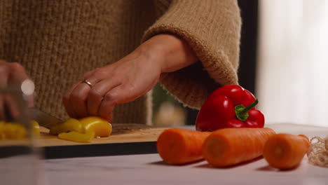 close up of woman at home in kitchen preparing healthy fresh vegetables for vegetarian or vegan meal slicing yellow pepper on board 4