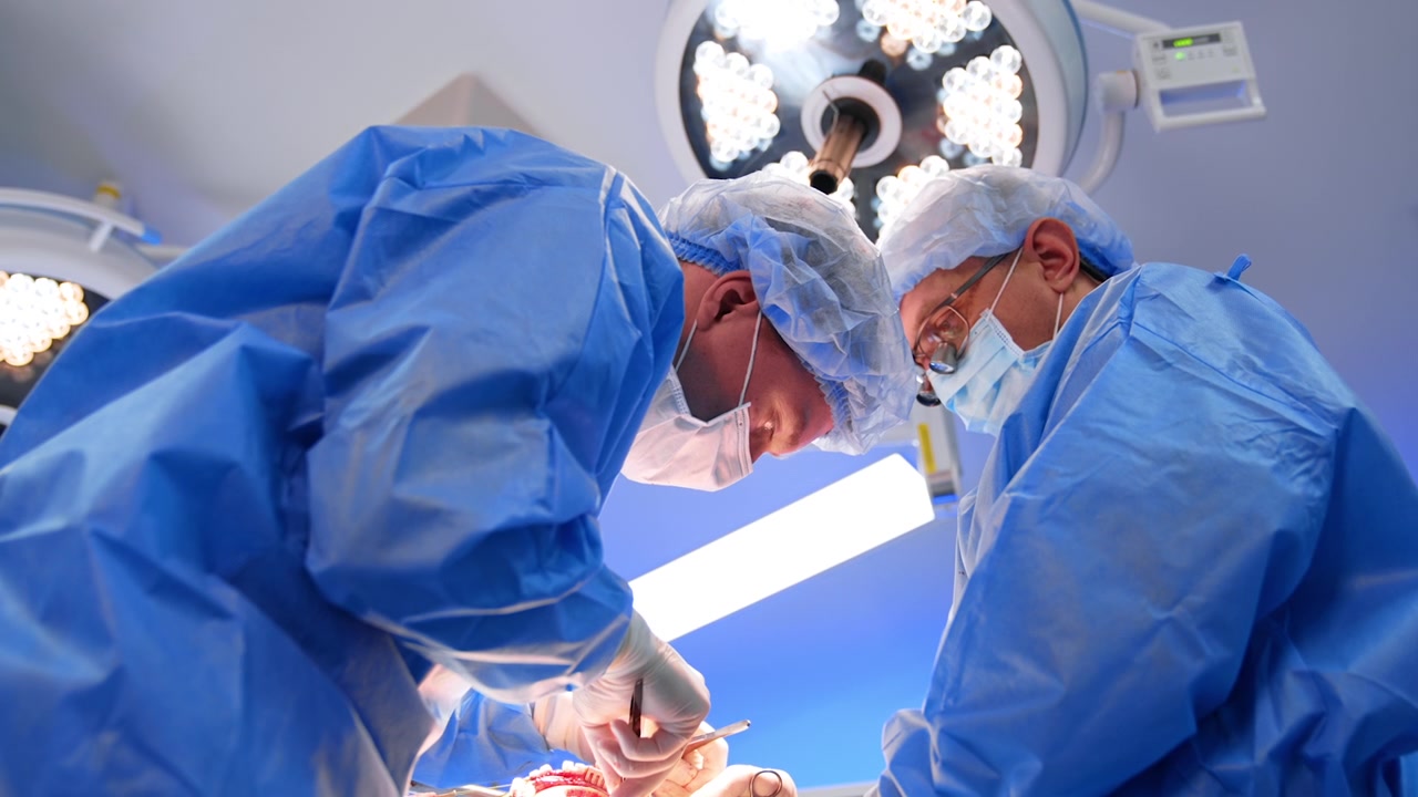 Medici chinati sul paziente che usano strumenti metallici. Vista dal basso sui chirurghi che eseguono l'operazione sotto la lampada rotonda.