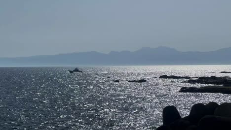 silhouetted rocks on a sparkling sea with boats cruising under a clear blue sky