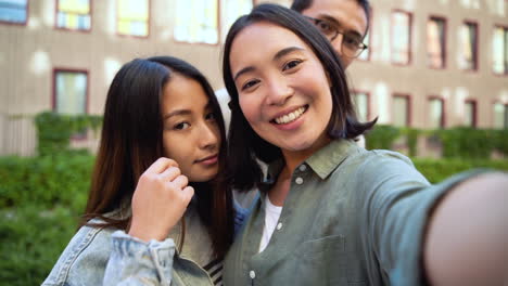 group of three young japanese friends looking at camera and taking selfie photos together