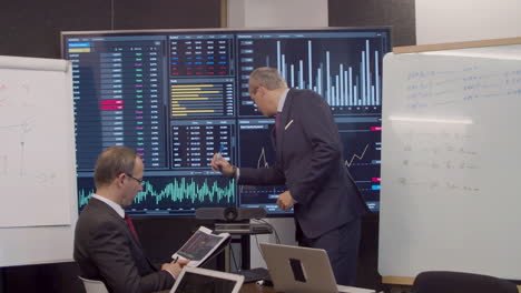 man pointing at screen with pen while having meeting in office with a businessman