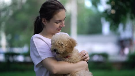 una mujer con un caniche de juguete caminando en un parque.