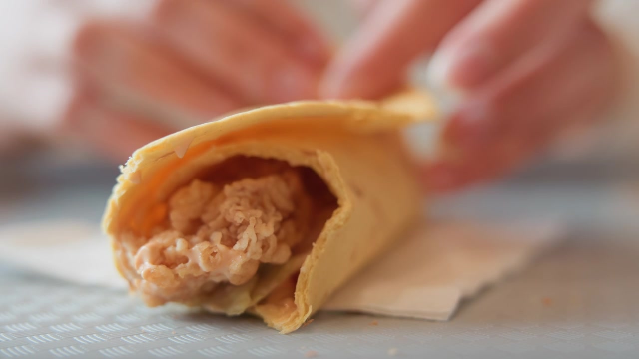 Tampilan dekat tangan menyelesaikan pembungkus tortilla dengan melipat dan menyelipkan roti pipih di sekitar daging suwir berkuah, dengan pembungkus diletakkan di atas serbet sementara jari-jari menekan tepi ke dalam untuk penyajian yang rapi