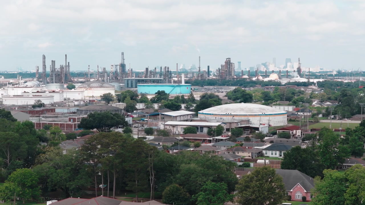 Luchtfoto van een grote olieraffinaderij en petrochemische fabriek die direct grenst aan een woonwijk met de skyline van New Orleans op de achtergrond. Chalmette, Louisiana, VS