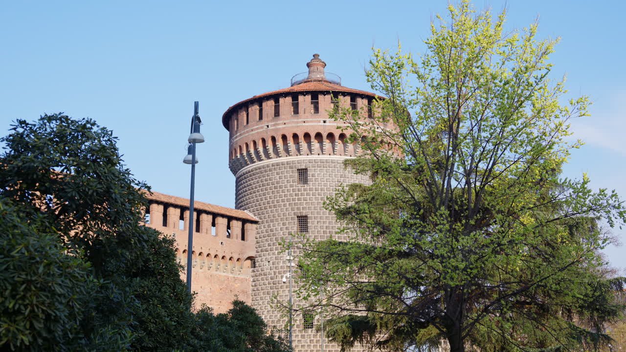 View of the Sforzesco Castle in Milan, Italy, surrounded by green trees on a blue sky background