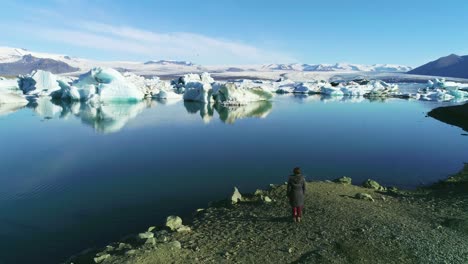 冰川湖沿岸的女人在北極的jokulsarlon冰川湖沿岸站立的空中圖像 - 冰川湖冰川