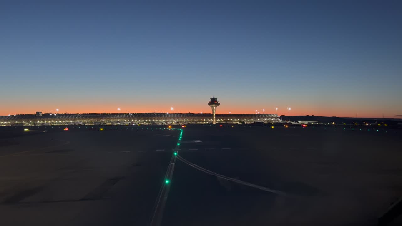 Pemandangan kokpit imersif saat melaju ke landasan pacu Bandara Madrid untuk lepas landas sesaat sebelum matahari terbit, dengan menara kontrol dan Terminal 4S di latar belakang.