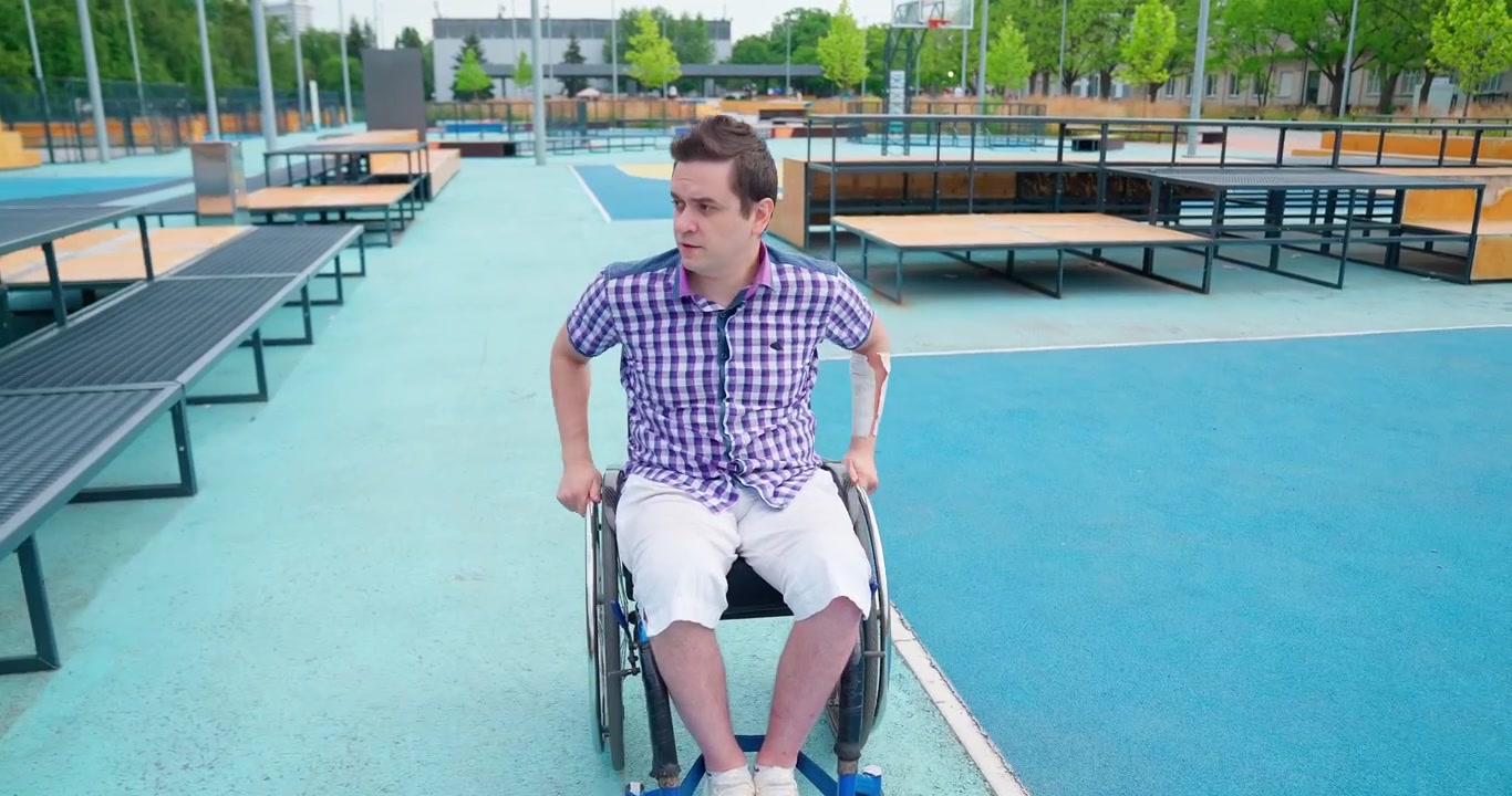 Young Man in Wheelchair Propelling Himself in a Modern Urban Park