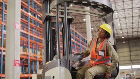 African-american-female-worker-wearing-safety-suit-and-sitting-in-turret-truck-in-warehouse