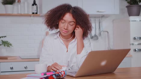 young african american woman inserts wireless headphones sits at kitchen table