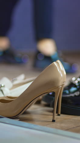diverse kinds of female shoes on the floor at foreground. woman in black jeans and shoes jumping at backdrop in blur. vertical video
