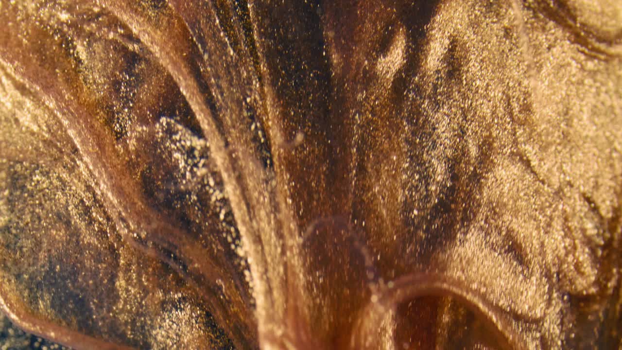 las partículas de tinta dorada fluyen en el agua como un caos colorido en el fondo negro