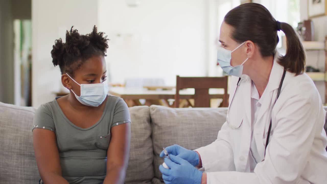 African american girl and caucasian female doctor wearing face masks, vaccinating