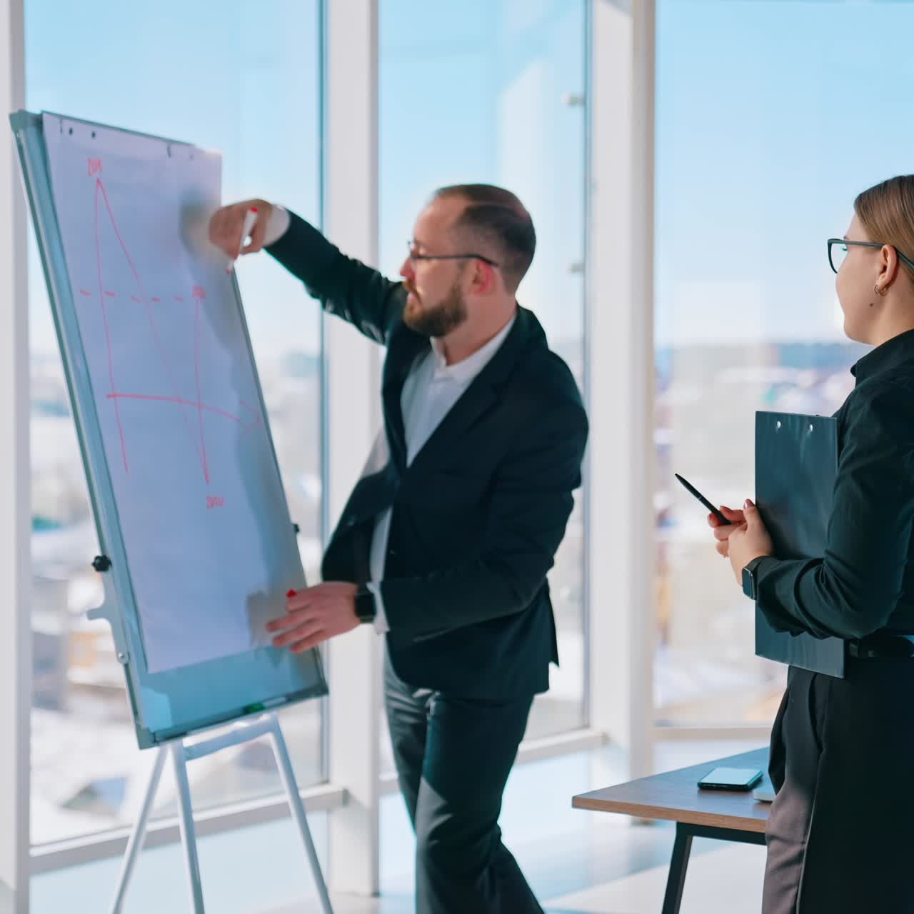 Business coworkers making about new blueprint. Successful man and smart woman in black suits working in office together. Panoramic windows background