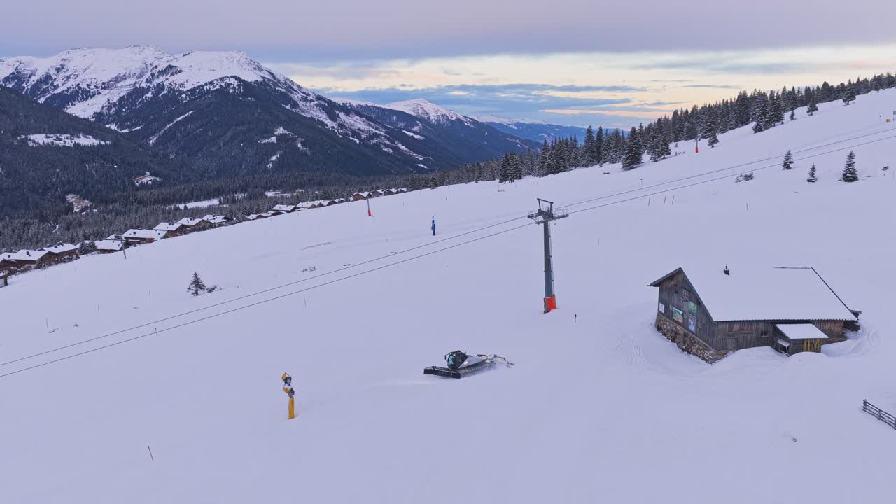 Dron zachycuje rolby upravující lyžařské sjezdovky v Zillertal Areně, Krimmlu a Königsleitenu, Rakousko, s zasněženými horami obklopujícími středisko.
