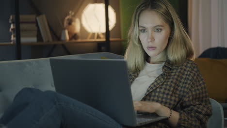 Woman working on laptop at night on a couch